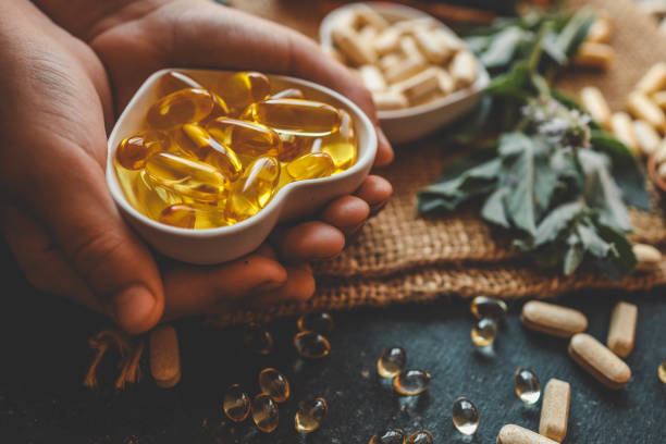 Hand holding a dish of softgel and herbal capsules beside fresh herbs